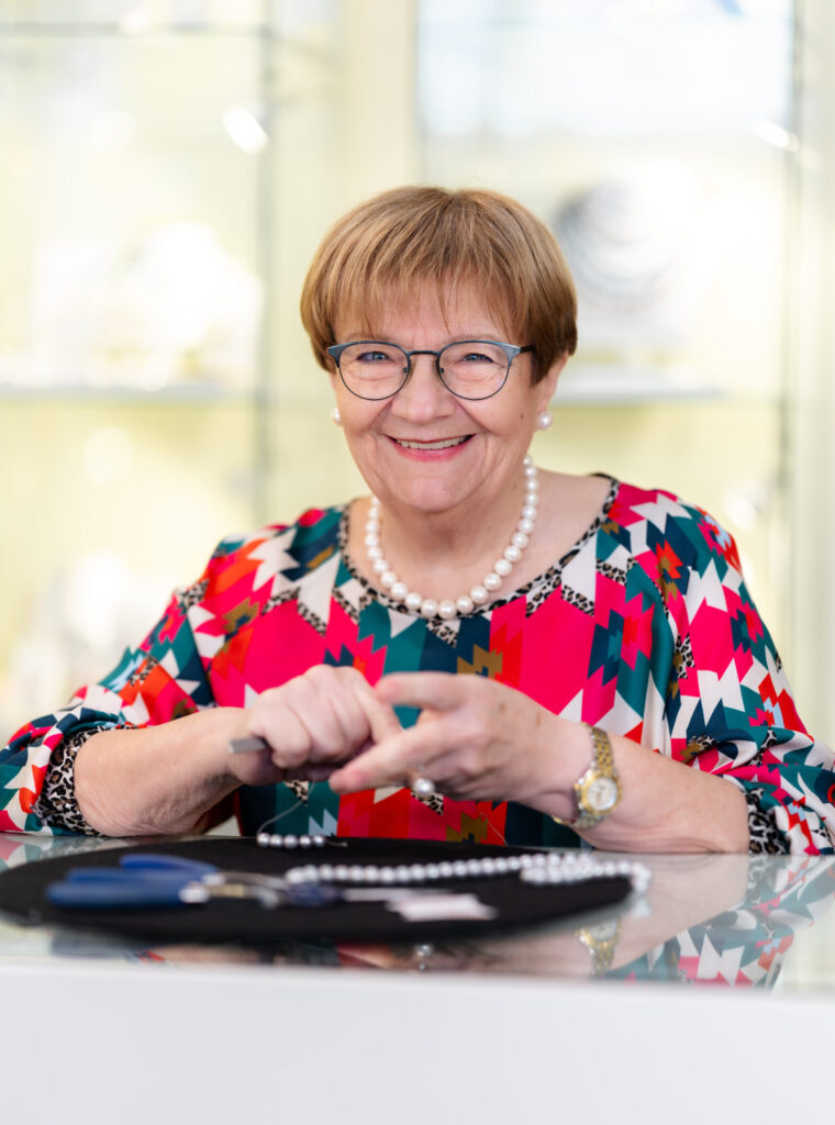 Die Eigentümerin lächelt in die Kamera vor ihr befindetet sich eine Perlenkette im aufbau